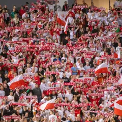 Tłum kibiców z szalikami "Polska" i flagami, emocjonujący doping podczas meczu, kiedy baraże o ekstraklasę.