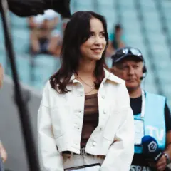 Maja Strzelczyk w białej kurtce, gotowa do pracy na stadionie. W tle widać ekipę telewizyjną.