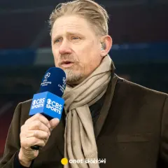 Antoni Schmeichel, z mikrofonem CBS Sports i szalikiem, komentuje mecz Ligi Mistrzów.