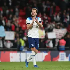 Harry Kane, w białej koszulce Anglii, klaszcze na tle trybun. Choć nie wiemy, ile lat ma Harry Kane, jego forma na boisku mówi sama za siebie.