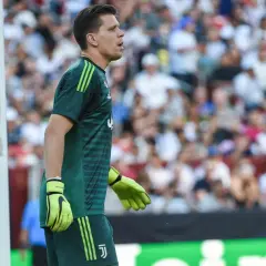 Bramkarz w zielonym stroju, z rękawicami na dłoniach, czeka na akcję. To jego **szczęsny wiek**, pełen determinacji i skupienia na boisku.
