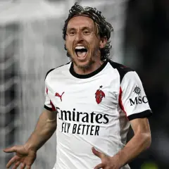 Piłkarz w białej koszulce z logo Milanu, z uniesionymi rękami i krzykiem radości. To moment triumfu w **luka modrić gry**.