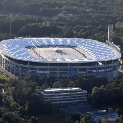 Stadion piłkarski otoczony drzewami, z charakterystycznym białym dachem.
