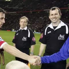 Piłkarz w czerwonej koszulce, Gary Neville, ściska dłoń rywalowi. Sędziowie obserwują.