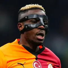 Piłkarz Osimhen w masce ochronnej na twarzy, w pomarańczowo-czerwonej koszulce z herbem Galatasaray.
