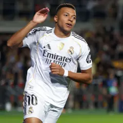 Piłkarz w białej koszulce Realu Madryt, z numerem 10, radośnie unosi rękę. To Kylian Mbappé, którego nazwisko pisze się właśnie tak.