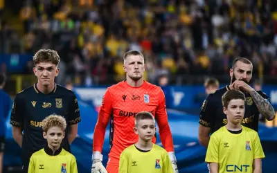 Bramkarz Lecha Poznań w pomarańczowej koszulce stoi obok młodych zawodników.