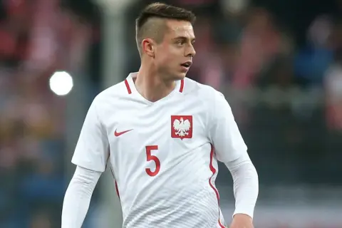 Piłkarz Borysiuk w białej koszulce z numerem 5 i godłem Polski.