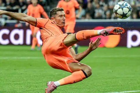 Piłkarz w pomarańczowym stroju wykonuje przewrotkę, celując w piłkę. Czy to on gra w finale Ligi Mistrzów?
