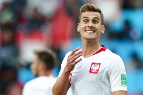 Piłkarz reprezentacji Polski z szerokim uśmiechem, jakby cieszył się z każdego wieku sukcesu. Biała koszulka z godłem orła.