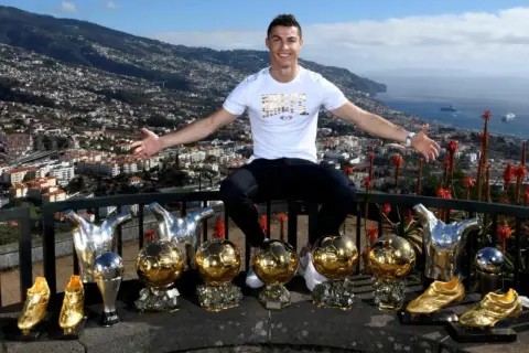 Cristiano Ronaldo z dumą prezentuje swoje liczne trofea, w tym Złote Piłki, na tle malowniczego krajobrazu Madery, swojego rodzinnego domu.