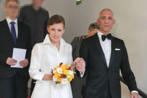 Szczęśliwa para młoda, Maciej i jego żona, idą schodami. Ona w białej sukni z bukietem, on w eleganckim smokingu.
