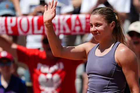 Maja Chwalińska, uśmiechnięta, macha do kibiców. W tle widać transparent z napisem "POLSKA".