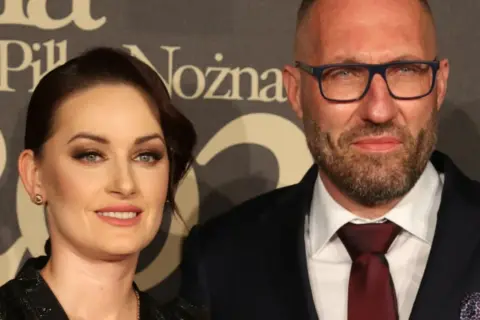 Marek Papszun z pierwszą żoną, uśmiechnięci, pozują do zdjęcia na tle napisu.