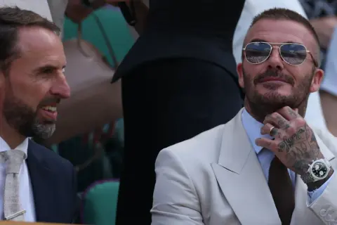 David Beckham, którego majątek robi wrażenie, w okularach przeciwsłonecznych i eleganckim jasnym garniturze, rozmawia z Garethem Southgate'em.