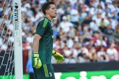 Bramkarz w zielonym stroju, z rękawicami na dłoniach, czeka na akcję. To jego **szczęsny wiek**, pełen determinacji i skupienia na boisku.