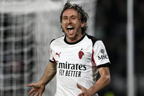 Piłkarz w białej koszulce z logo Milanu, z uniesionymi rękami i krzykiem radości. To moment triumfu w **luka modrić gry**.