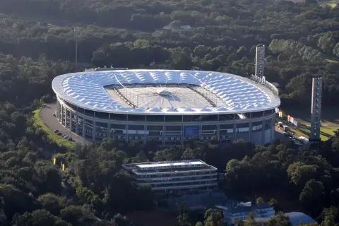 Stadion piłkarski otoczony drzewami, z charakterystycznym białym dachem.