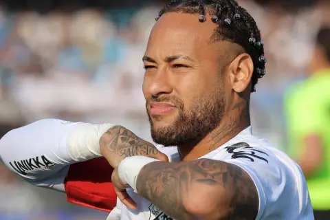 Neymar, z charakterystycznymi warkoczykami i tatuażami, w białej koszulce. Jego majątek budowany jest na boisku i poza nim.