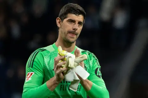 Thibaut Courtois w zielonej koszulce bramkarskiej, trzymający rękawice, z wyrazem twarzy sugerującym ból po kontuzji.