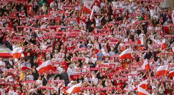 Tłum kibiców z szalikami "Polska" i flagami, emocjonujący doping podczas meczu, kiedy baraże o ekstraklasę.