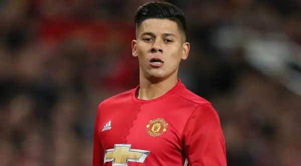 Piłkarz w czerwonej koszulce Manchester United, z logo klubu i Adidasa. Rojo wiek, skupiony na boisku.