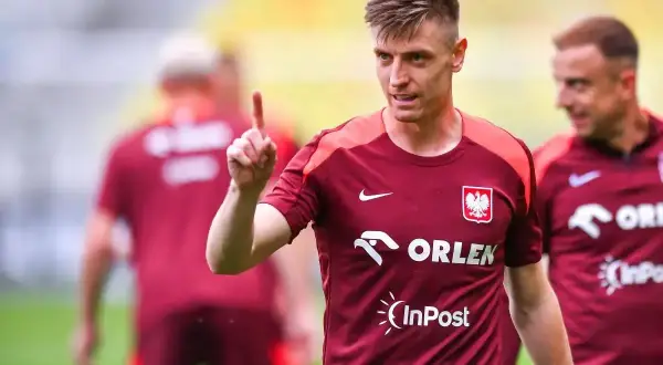 Krzysztof Piątek w koszulce reprezentacji Polski z logo Orlen i InPost, podnoszący palec. Jego zarobki budzą zainteresowanie.
