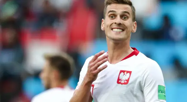 Piłkarz reprezentacji Polski z szerokim uśmiechem, jakby cieszył się z każdego wieku sukcesu. Biała koszulka z godłem orła.