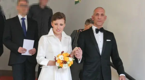 Szczęśliwa para młoda, Maciej i jego żona, idą schodami. Ona w białej sukni z bukietem, on w eleganckim smokingu.