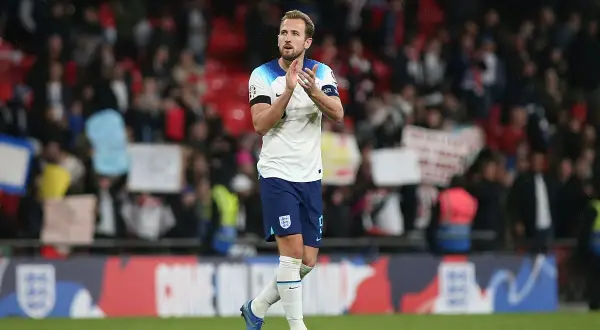 Harry Kane, w białej koszulce Anglii, klaszcze na tle trybun. Choć nie wiemy, ile lat ma Harry Kane, jego forma na boisku mówi sama za siebie.