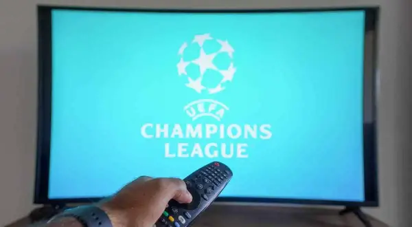 Ręka z pilotem szuka, gdzie transmisja Ligi Mistrzów. Na ekranie logo UEFA Champions League.