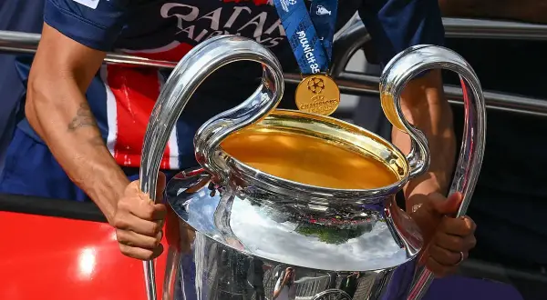Piłkarz trzyma Puchar Ligi Mistrzów, marząc o tym, kto wygra ligę mistrzów. Złoty medal wisi na jego szyi.