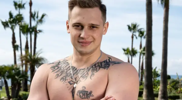 Daniel Majewski, młody mężczyzna z tatuażami na klatce piersiowej, pozuje na tle palm i błękitnego nieba.