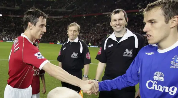 Piłkarz w czerwonej koszulce, Gary Neville, ściska dłoń rywalowi. Sędziowie obserwują.