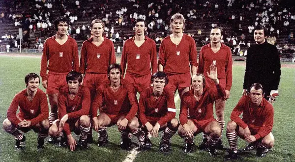 Znani piłkarze reprezentacji Polski w czerwonych strojach pozują na boisku.