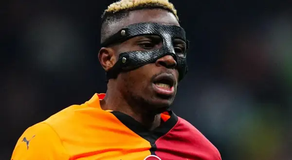 Piłkarz Osimhen w masce ochronnej na twarzy, w pomarańczowo-czerwonej koszulce z herbem Galatasaray.