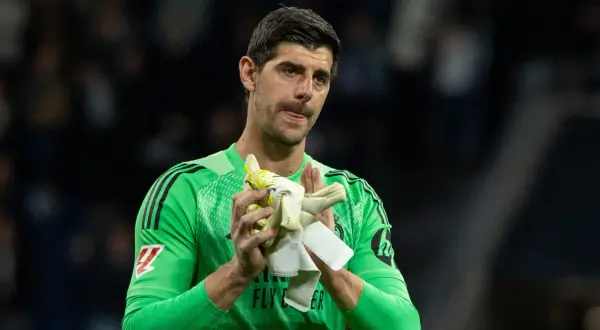 Thibaut Courtois w zielonej koszulce bramkarskiej, trzymający rękawice, z wyrazem twarzy sugerującym ból po kontuzji.