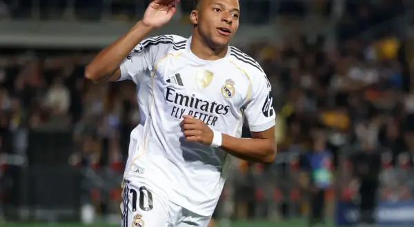 Piłkarz w białej koszulce Realu Madryt, z numerem 10, radośnie unosi rękę. To Kylian Mbappé, którego nazwisko pisze się właśnie tak.