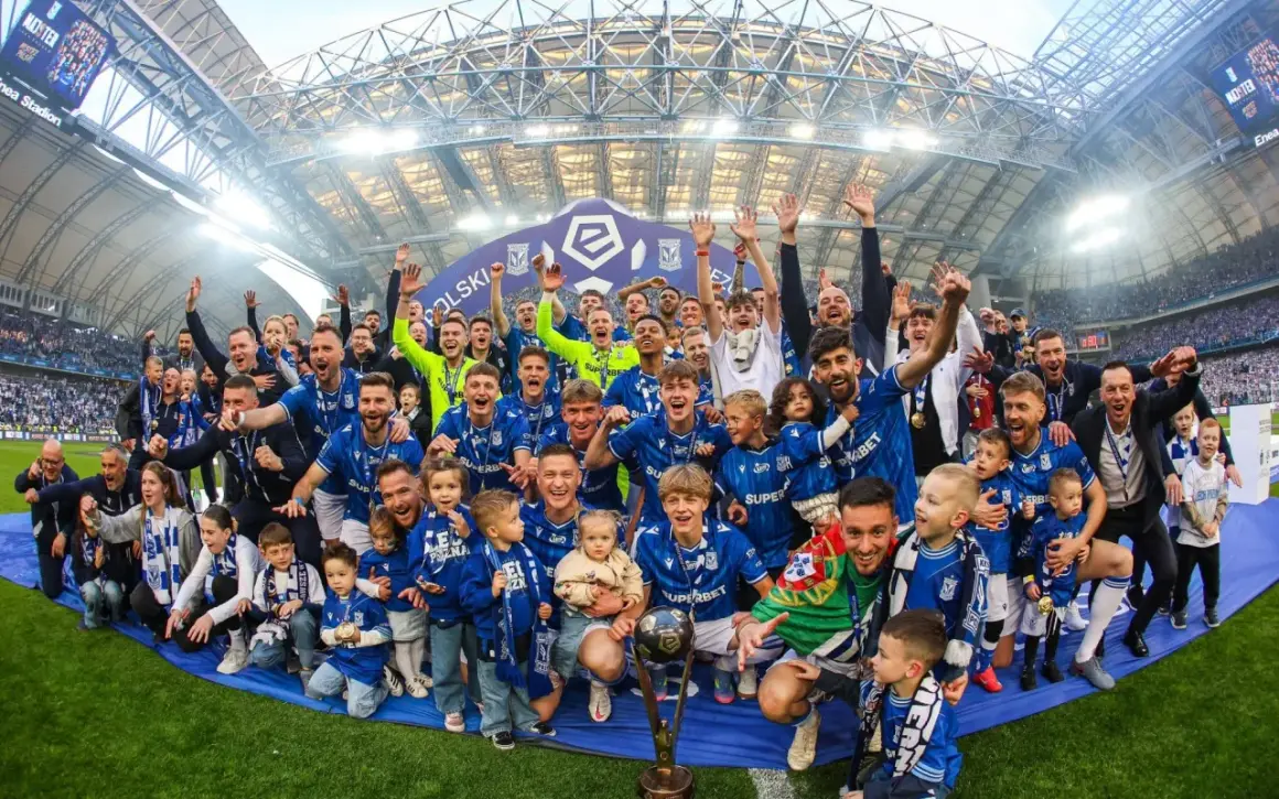 Byli piłkarze Lecha Poznań świętują z pucharem i dziećmi na murawie stadionu.