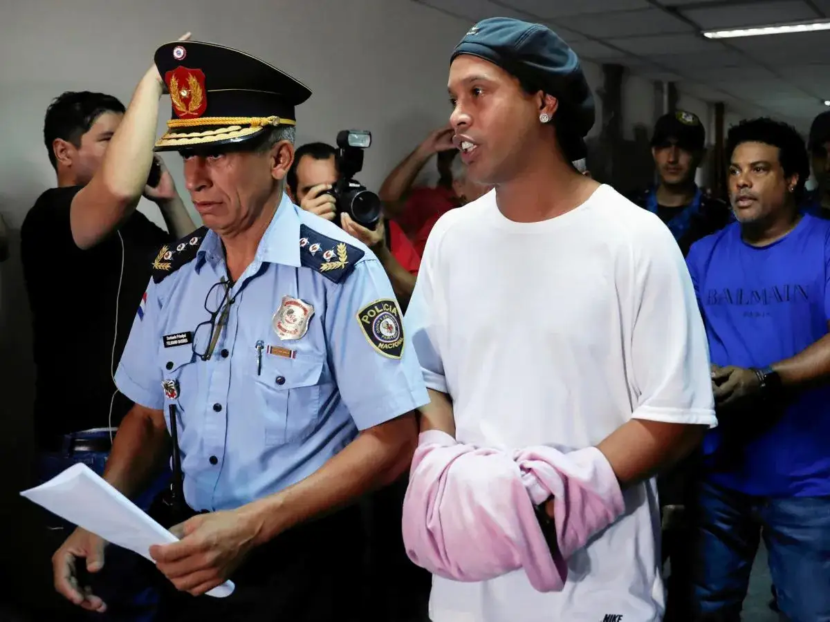 Ronaldinho w areszcie, prowadzony przez policjanta. Słynny piłkarz trafił do więzienia w Paragwaju.