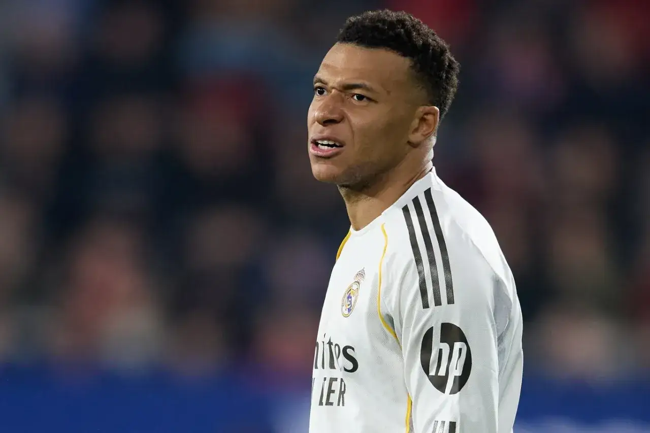 Mbappé, młody piłkarz, w białej koszulce Realu Madryt, zamyślony na boisku.