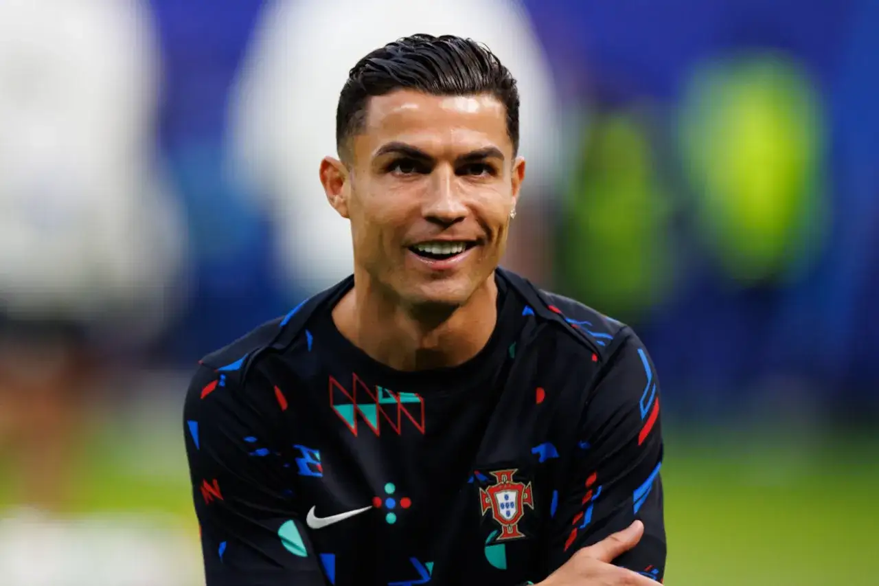 Uśmiechnięty Cristiano Ronaldo w czarnej koszulce z herbem Portugalii. Jego majątek to wynik ciężkiej pracy i talentu.