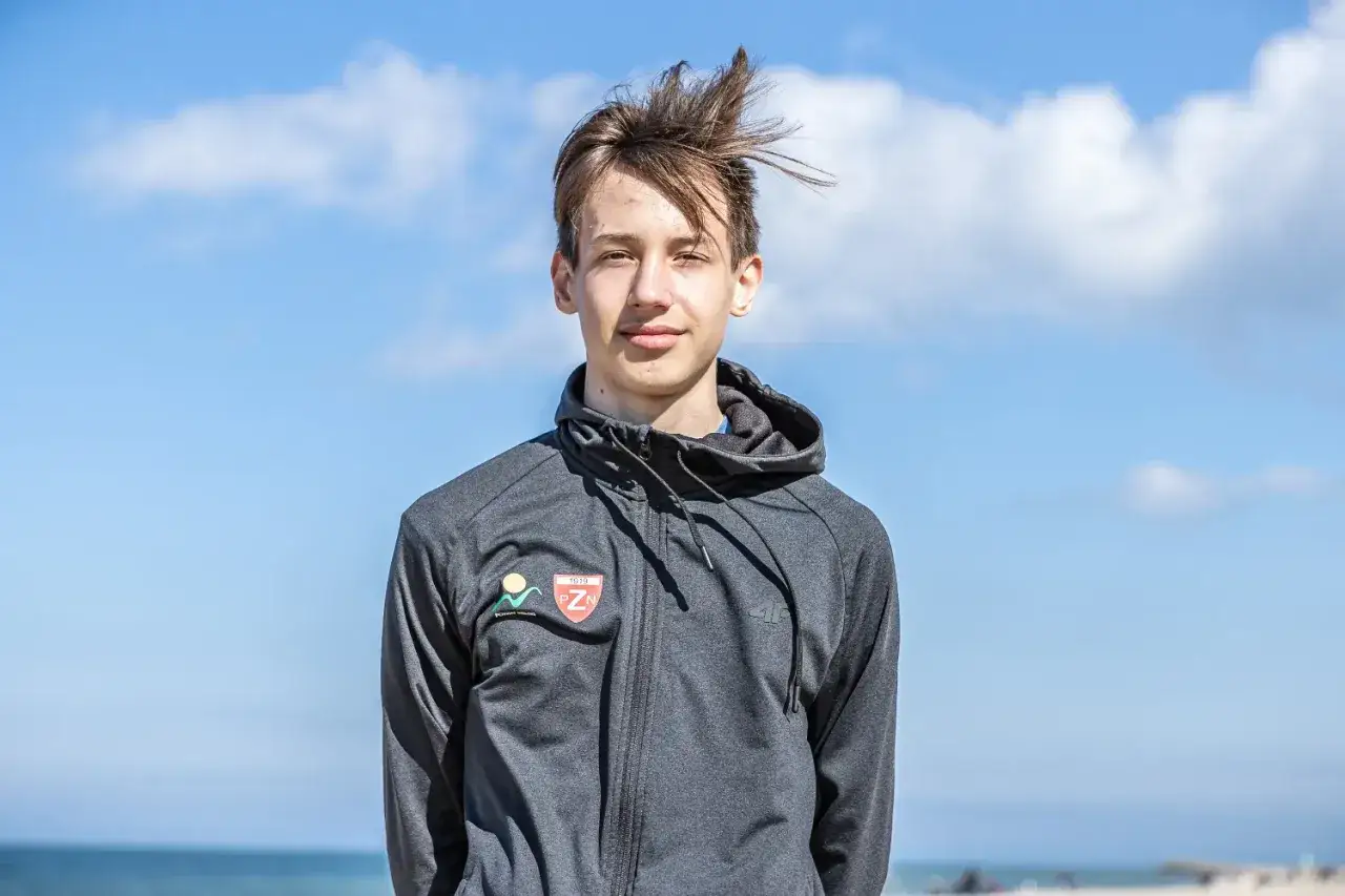 Kacper Tomasiak, młody sportowiec, na tle błękitnego nieba i morza. Jego wiek to około 16-18 lat.