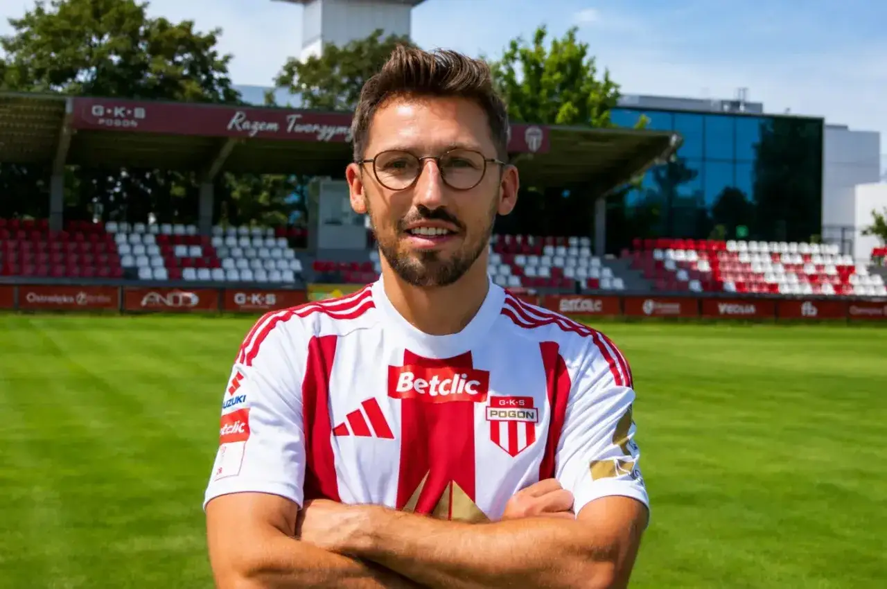 Piłkarz w koszulce GKS Pogoń Szczecin, w jakim klubie gra, pozuje na tle stadionu.