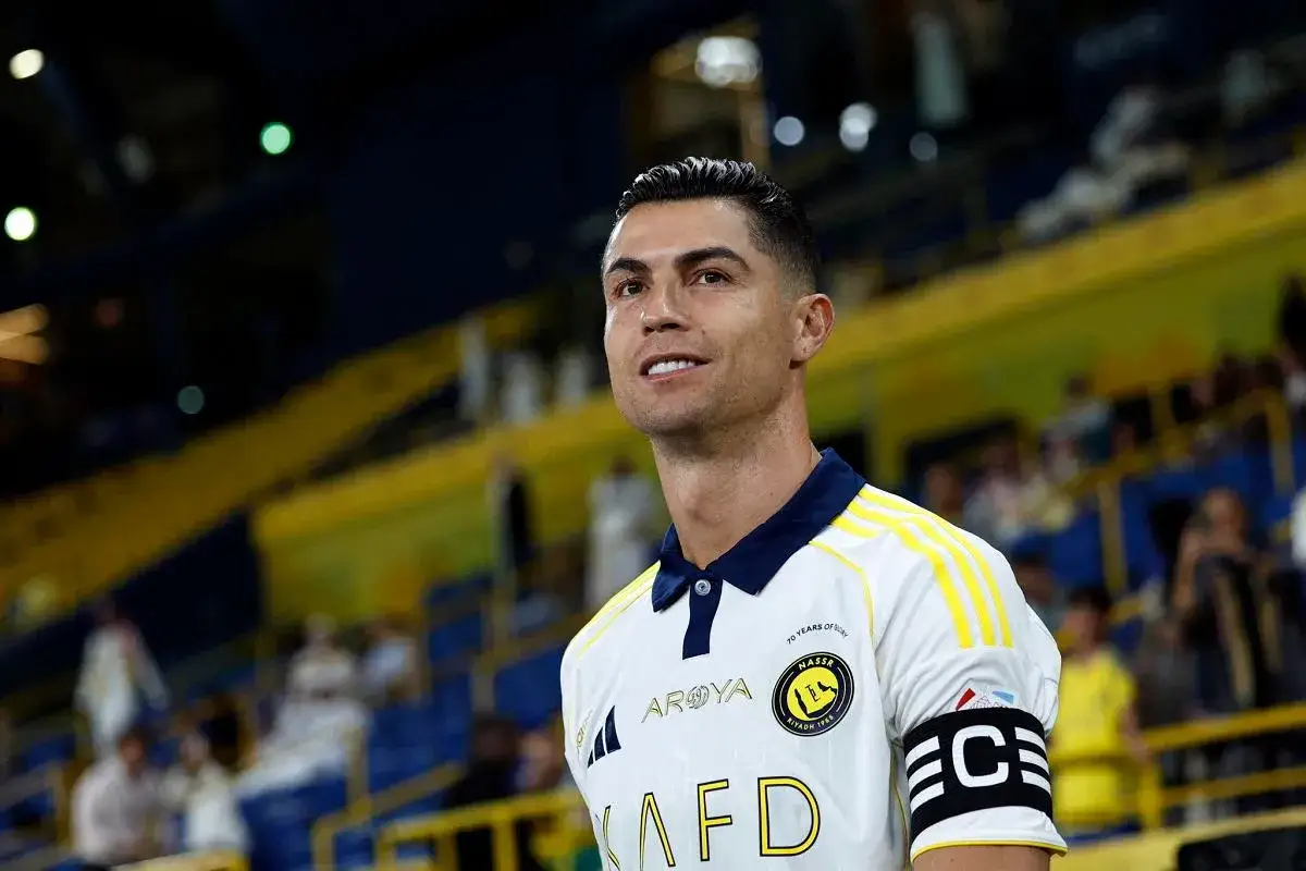 Ronaldo piłkarz w białej koszulce z żółtymi pasami, na tle trybun stadionu.