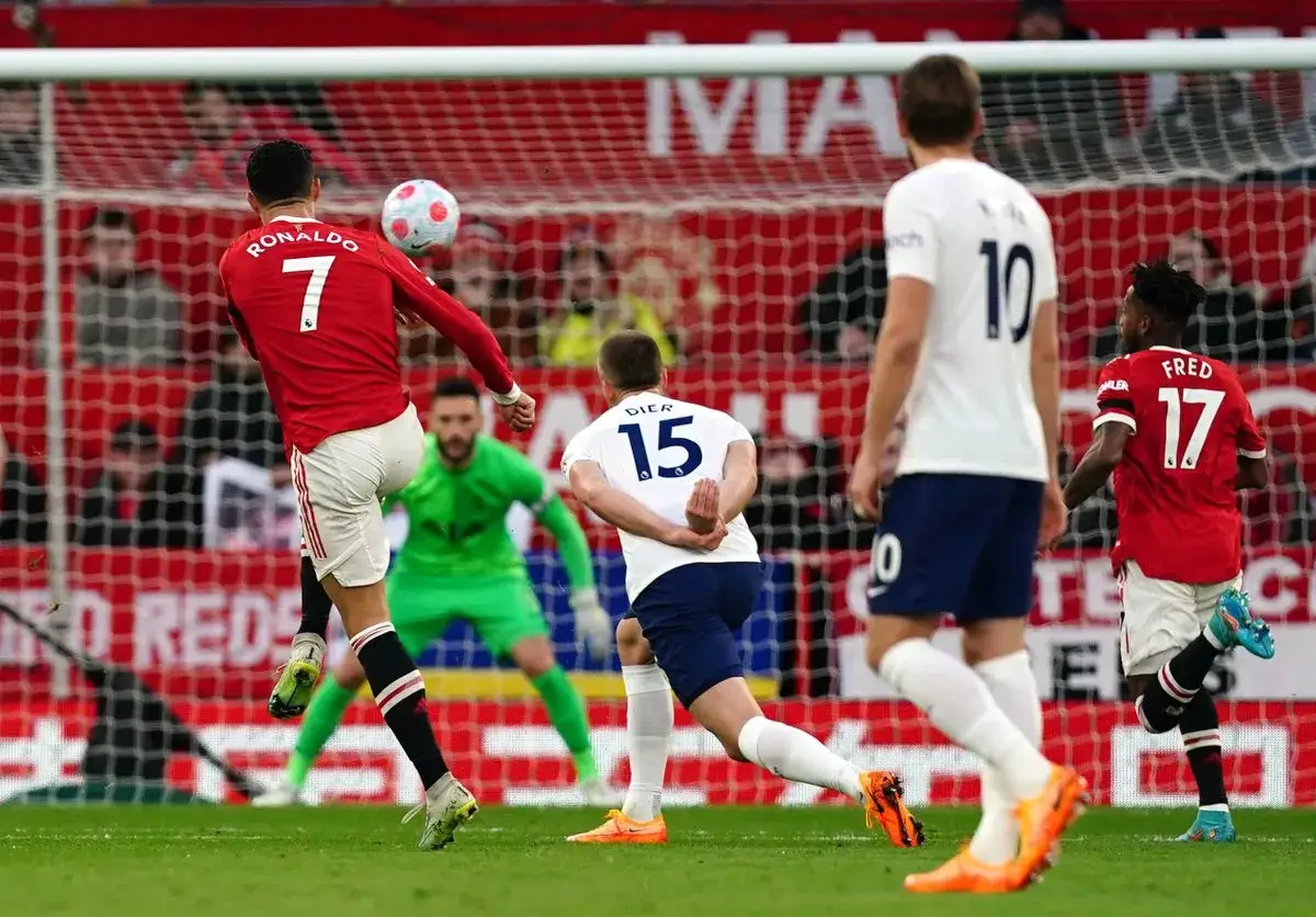 Piłkarz Ronaldo w czerwonej koszulce z numerem 7 wykonuje strzał głową. Jego wzrost pozwala mu na takie akcje. Bramkarz w zielonym stroju jest gotowy do obrony.