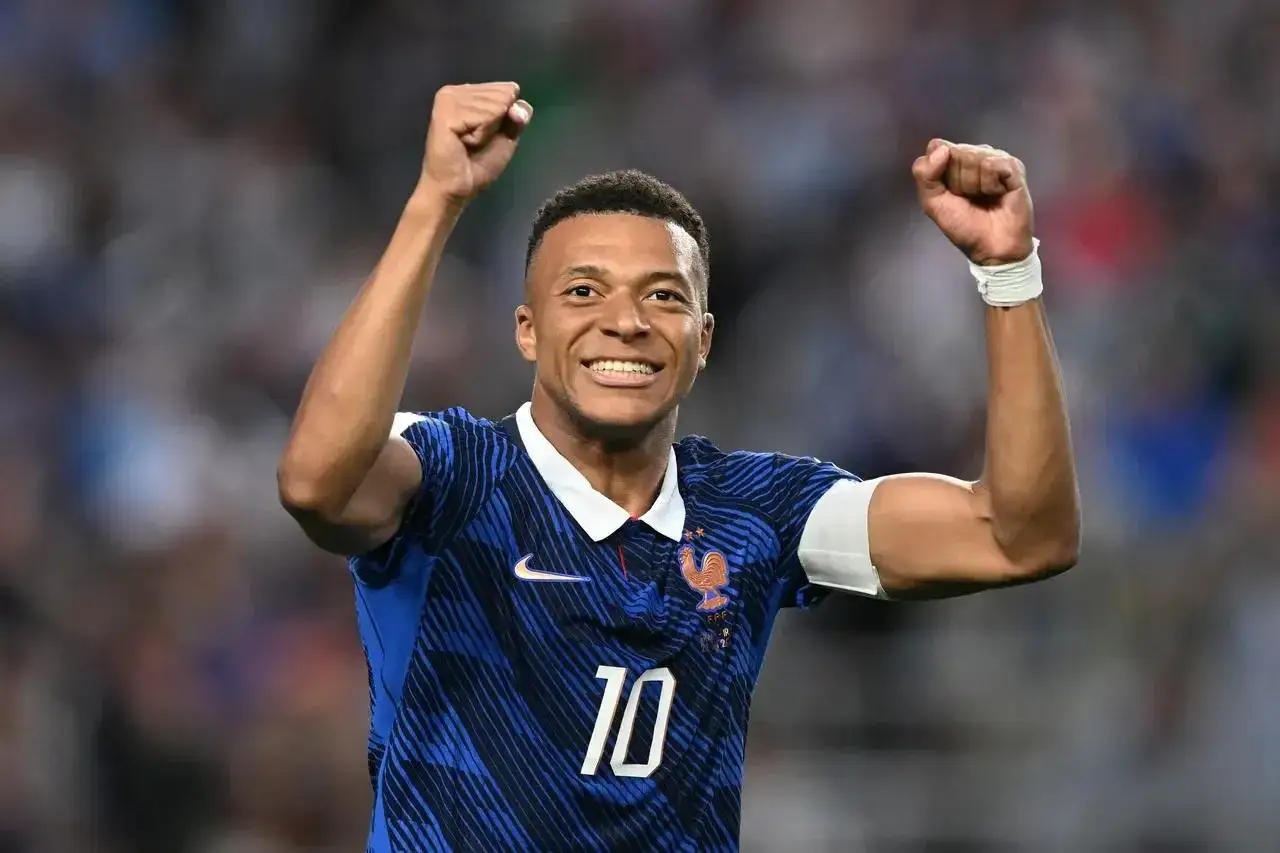 Kylian Mbappé w niebieskiej koszulce z numerem 10, świętuje zwycięstwo. Wszyscy zastanawiają się, ile lat ma Mbappé, a on wciąż zachwyca na boisku.
