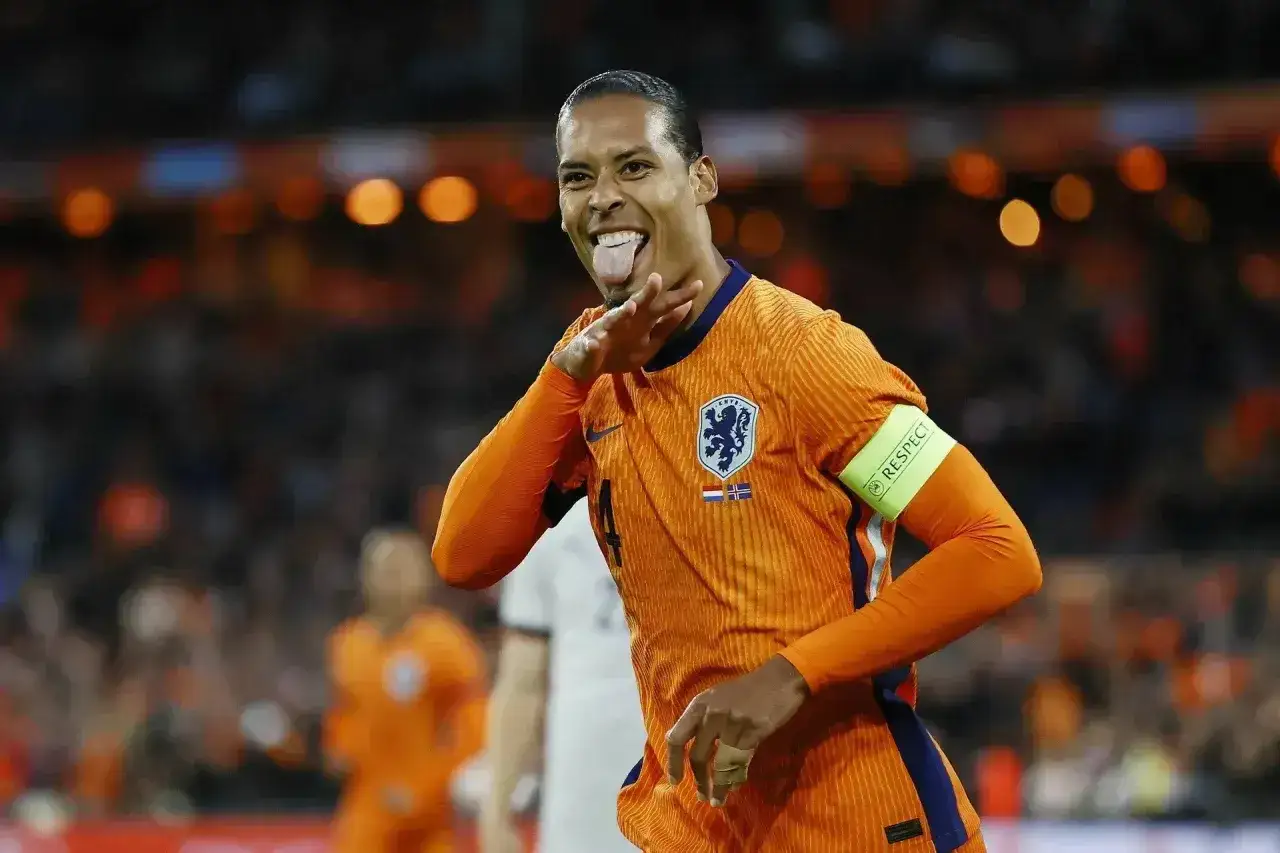 Virgil van Dijk, znany ze swojego imponującego wzrostu, w pomarańczowej koszulce reprezentacji Holandii, radośnie pokazuje język.