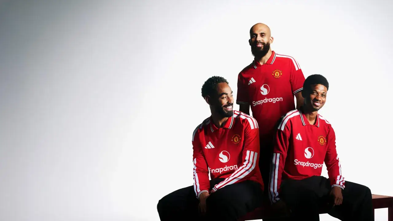 Trzech piłkarzy Manchesteru United w czerwonych koszulkach z logo Snapdragon pozuje do zdjęcia.