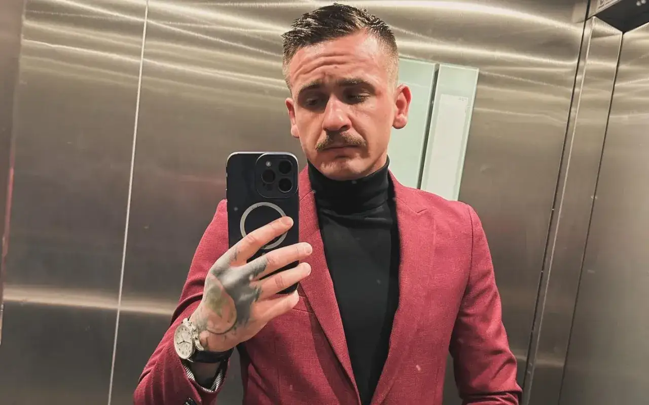 Mężczyzna w garniturze i golfie robi sobie selfie w windzie. Wiek tuszol.